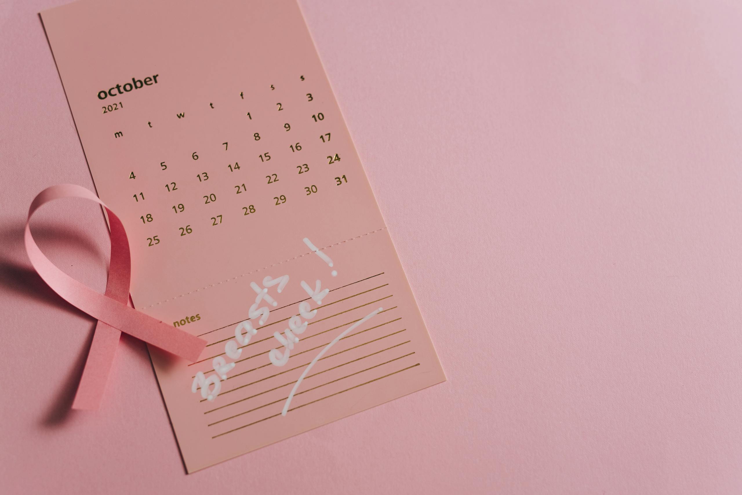 Pink ribbon on a calendar page for Breast Cancer Awareness, focused on health reminder in October.